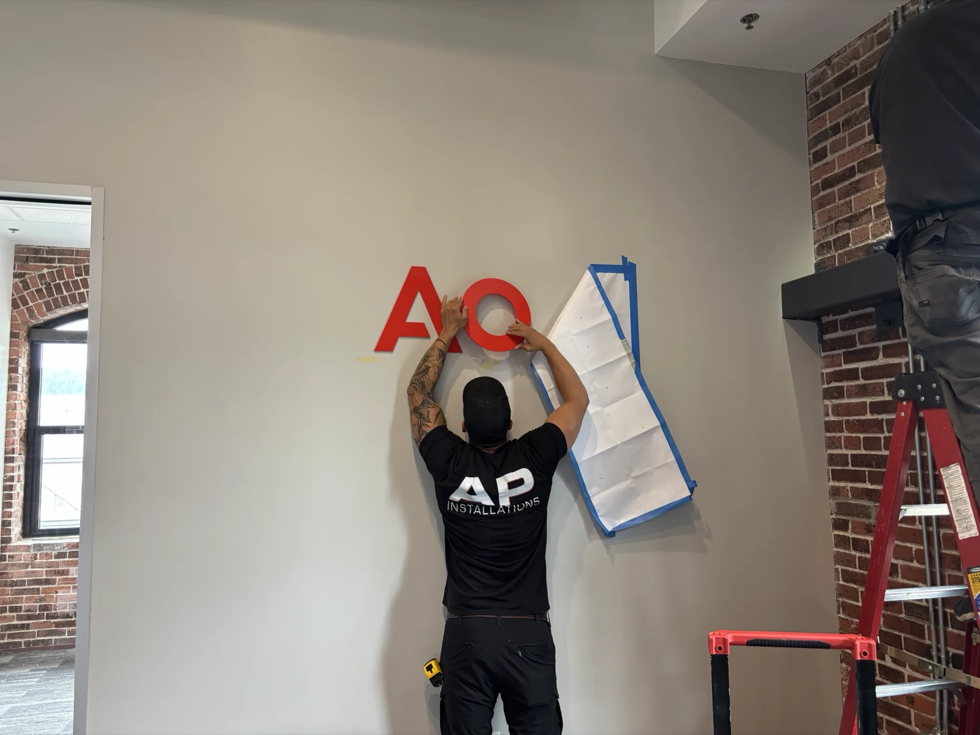 AP Installations installer applying red AON dimensional wall lettering in a commercial office